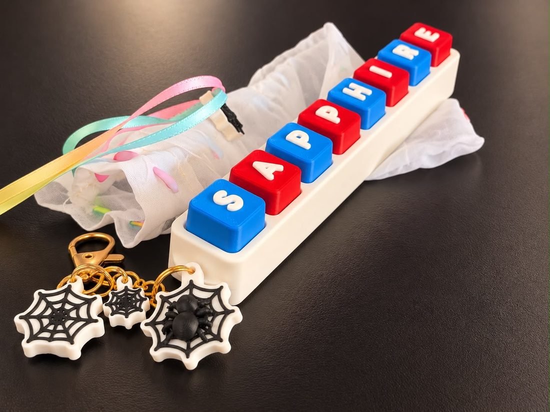 Name clicker with red and blue keys spelling Sapphire, next to web charms and a sheer gift bag
